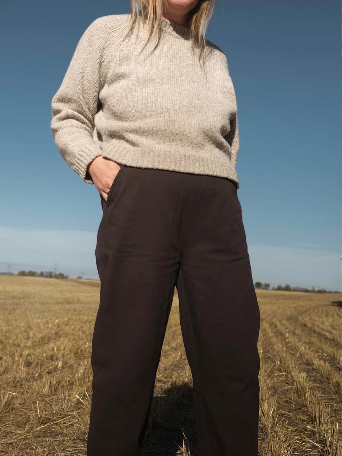 Person wearing The Woodland Sweater and dark pants standing in a field with a clear blue sky.