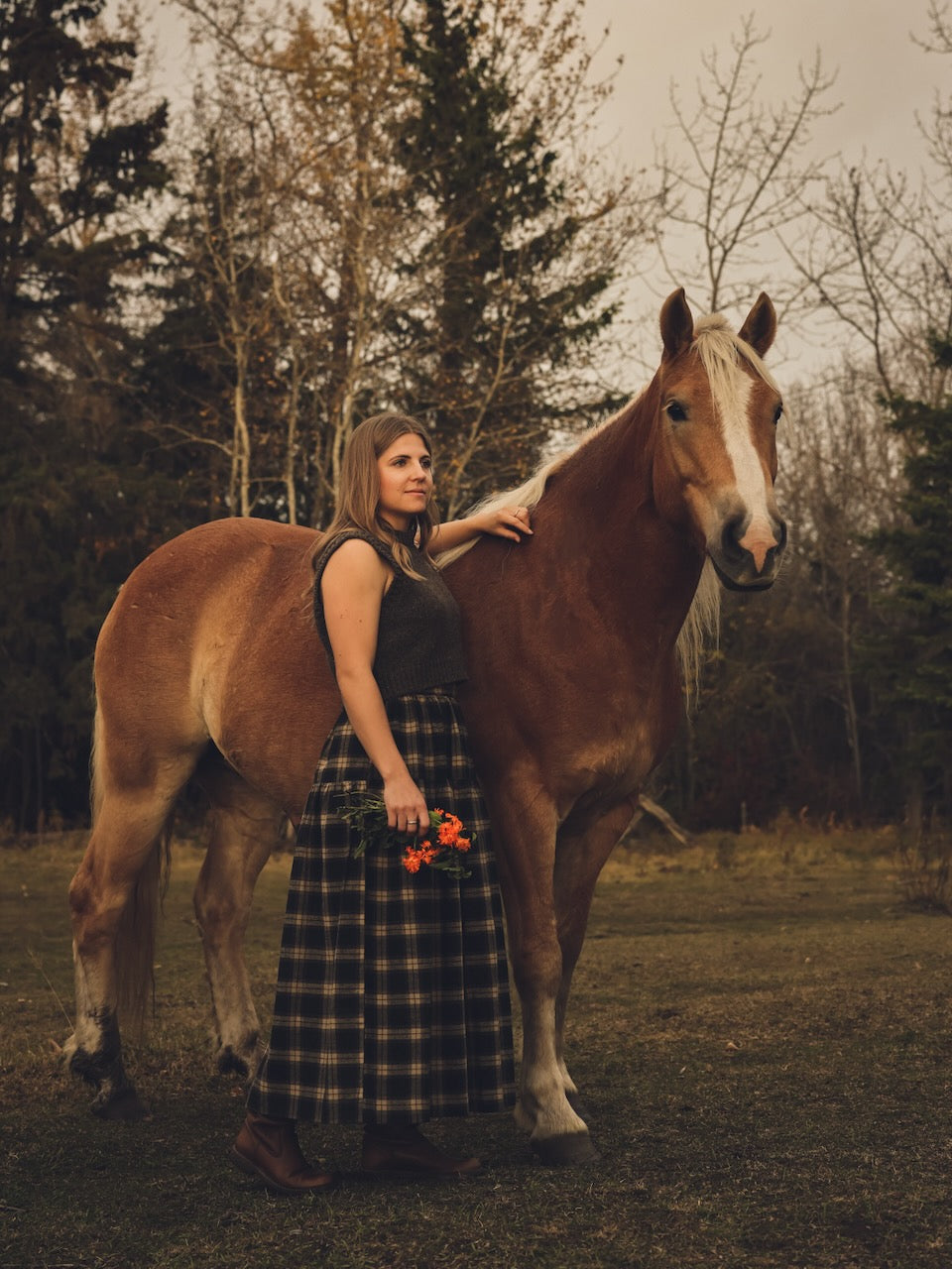 Woman standing next to a horse in a forested area