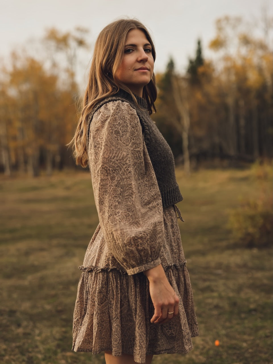 Woman in a patterned dress standing in a field with trees in the background